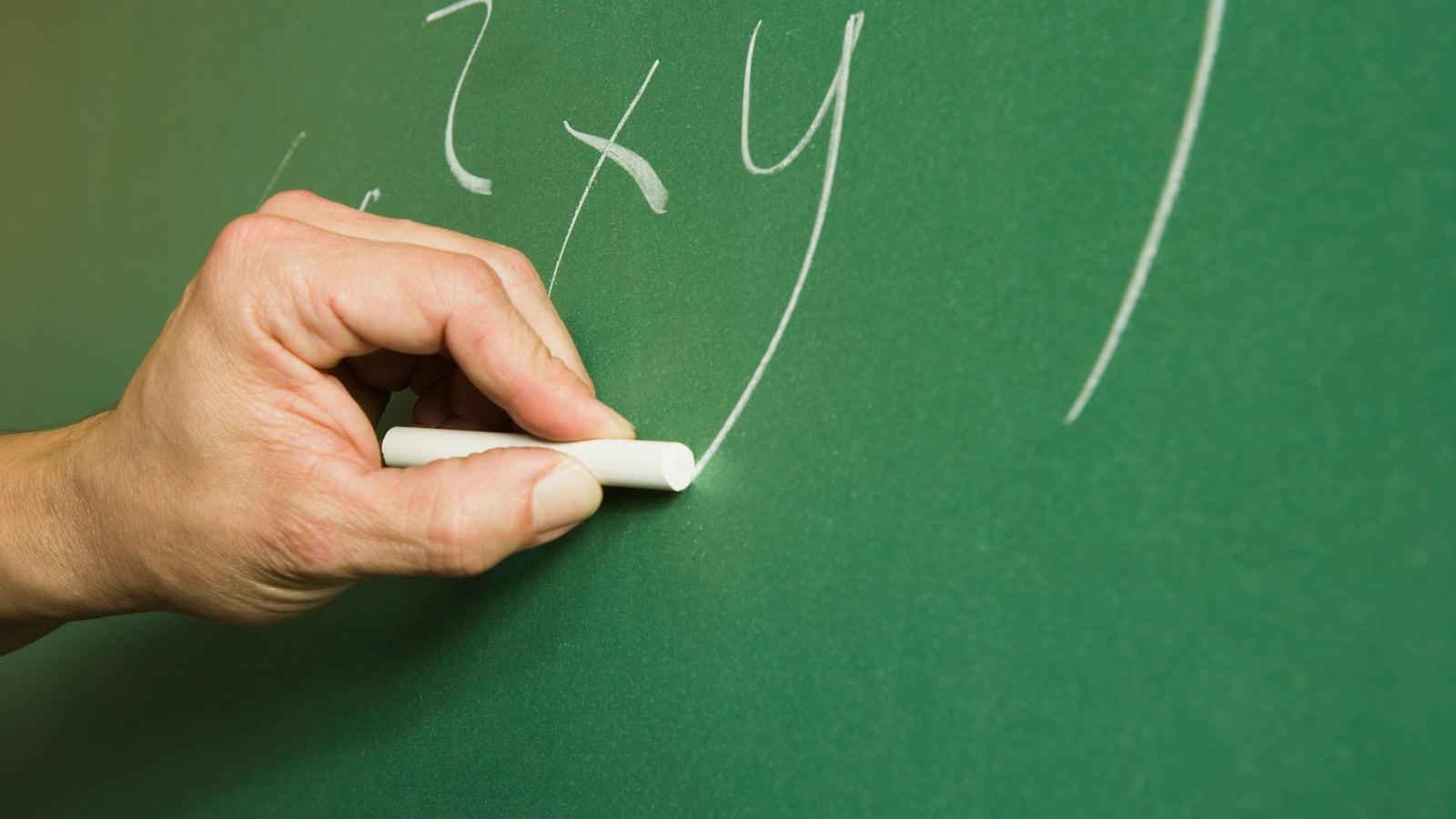 A teacher writes an algebraic equation on a green chalkboard