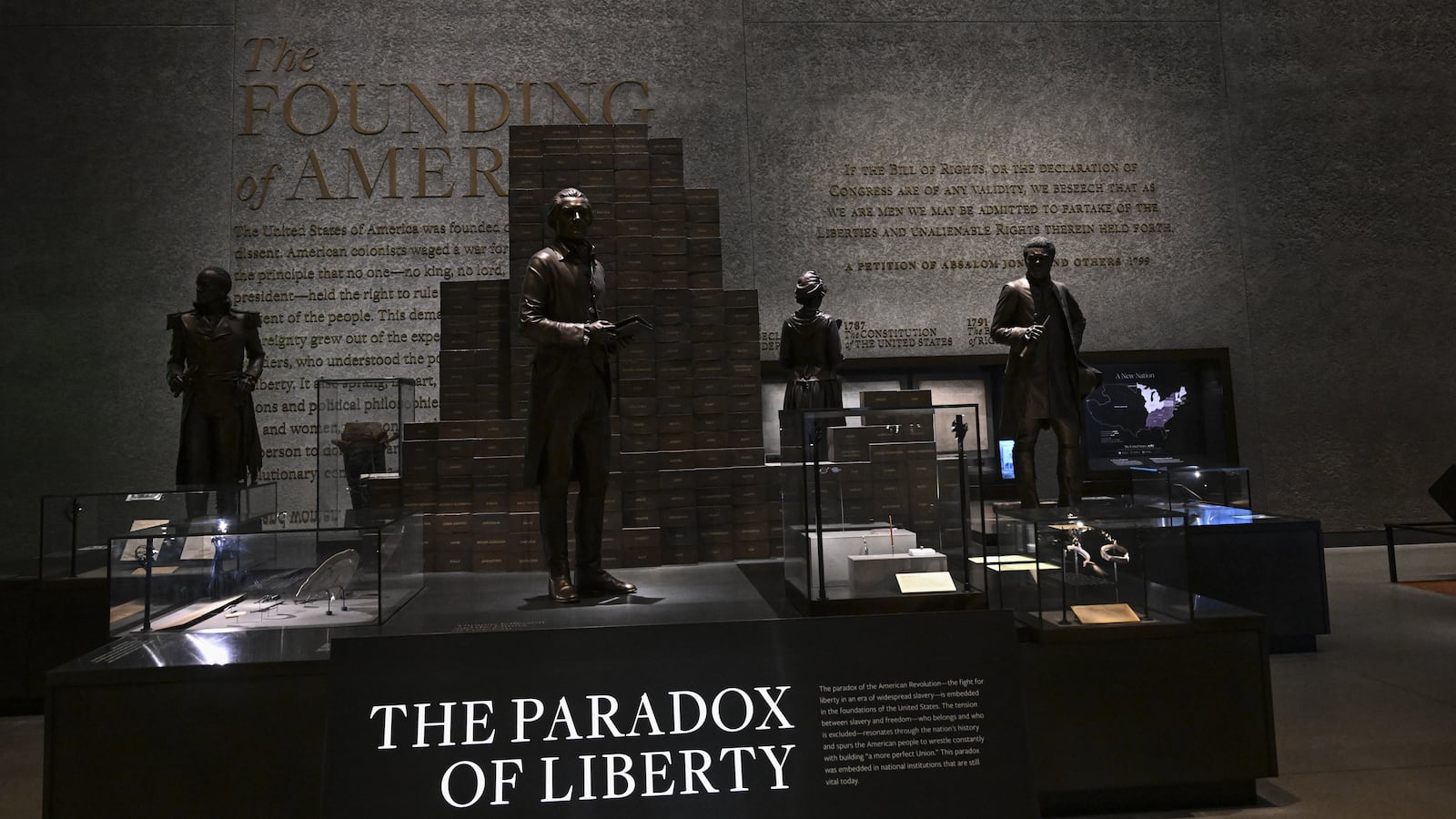 A hunk of wood and metal bar sit in the center of a near pitch dark room in the basement of the National Museum of African American History and Culture. A sign reads, “The Paradox of Liberty.”