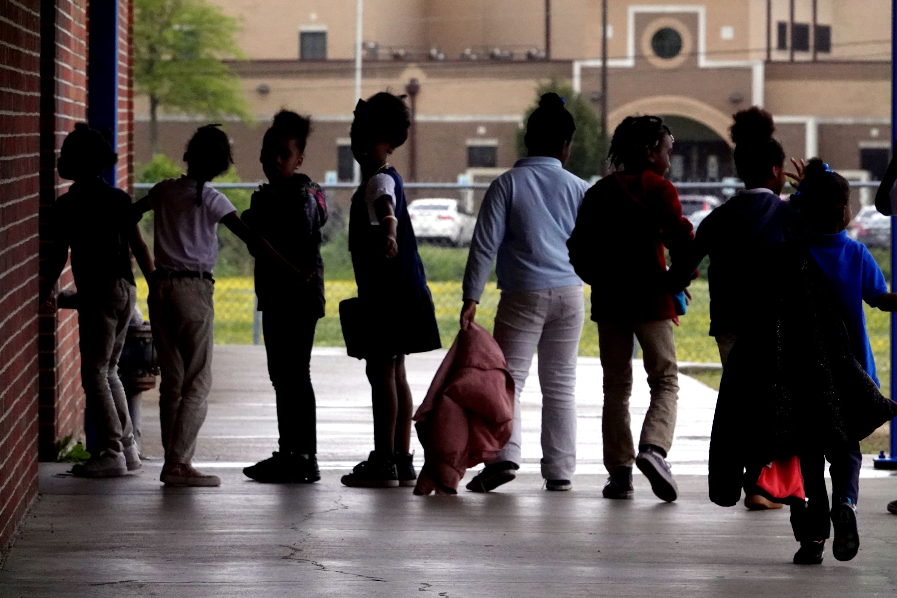 Young students stand in a line outside of a school building.