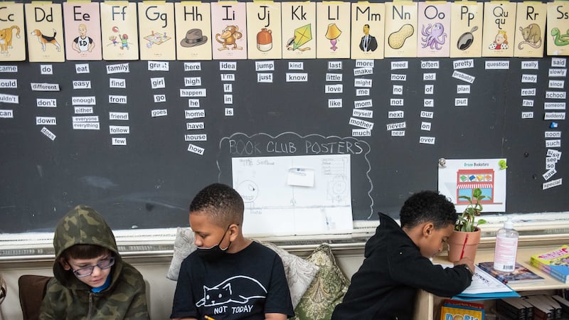 Three students sit with work in front of a chalkboard.