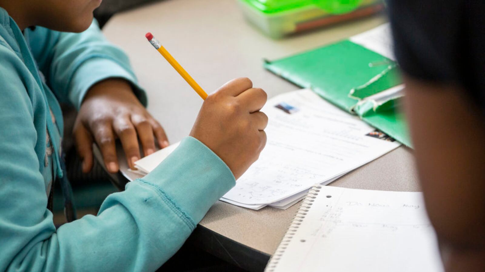 A student writes on a piece of paper at their desk.