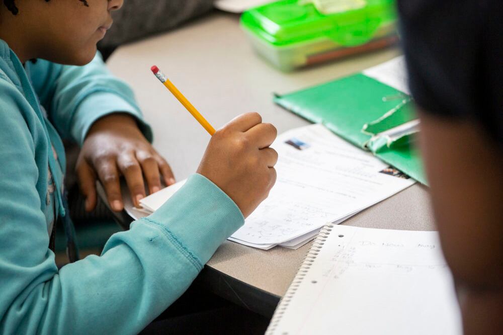 A student writes on a piece of paper at their desk.