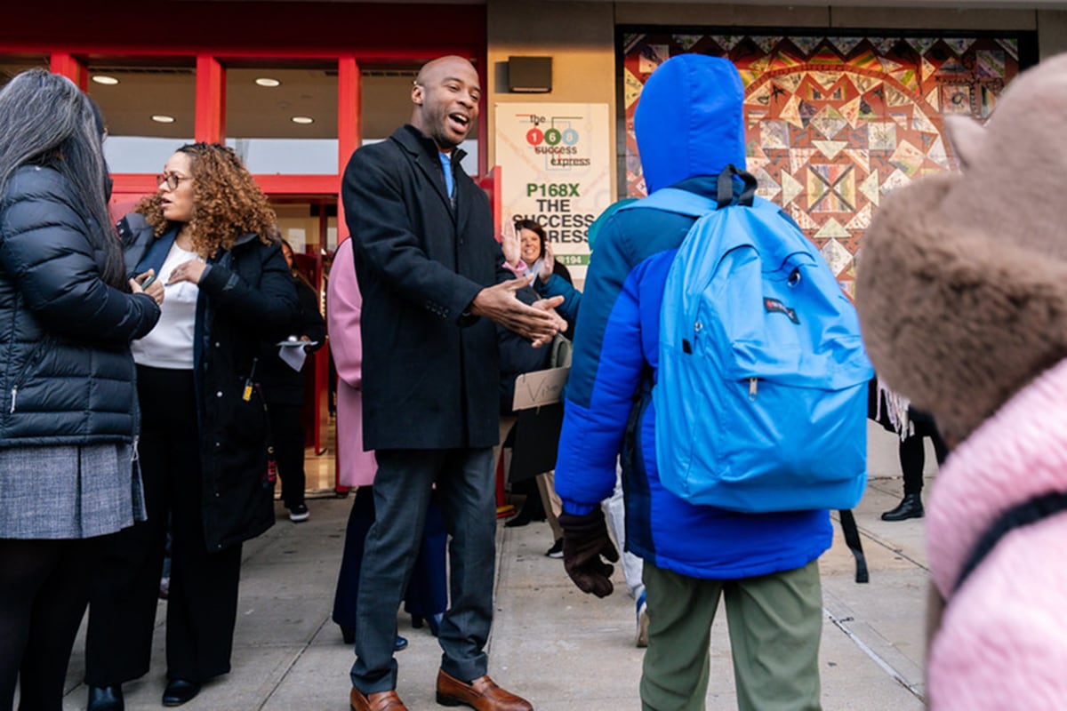 A man in a dark coat reaches to shake hands with a student.