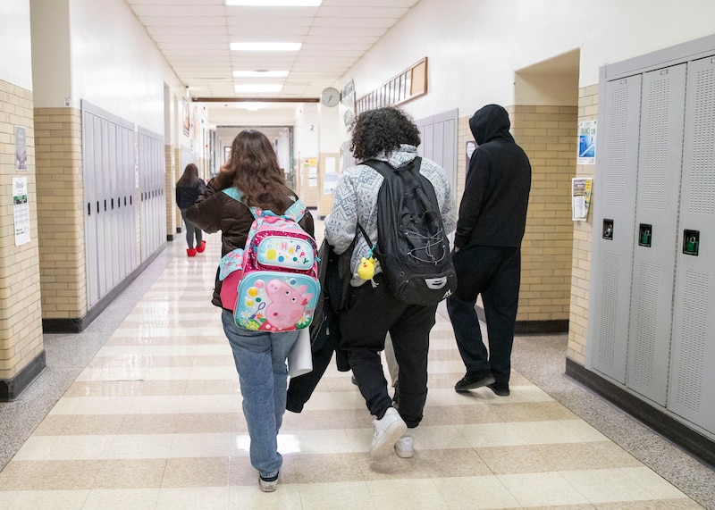 A photograph of high school students walking down a hallway with lockers on each side.