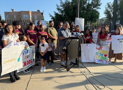 A group of adults and students stand outside holding signs.