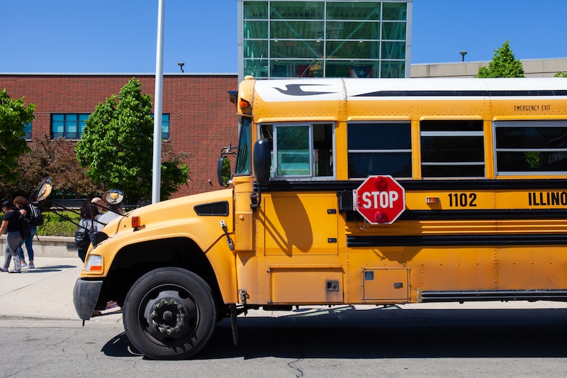A yellow school bus is parked near the front entrance of a school building.