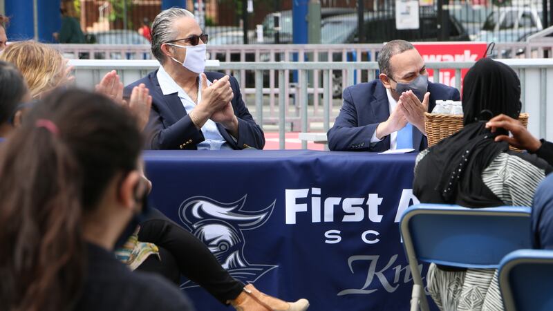 Newark schools Superintendent Roger León sits beside Newark Teachers Union President John Abeigon at a table covered in a blue cloth. Both men are clapping and wearing masks.