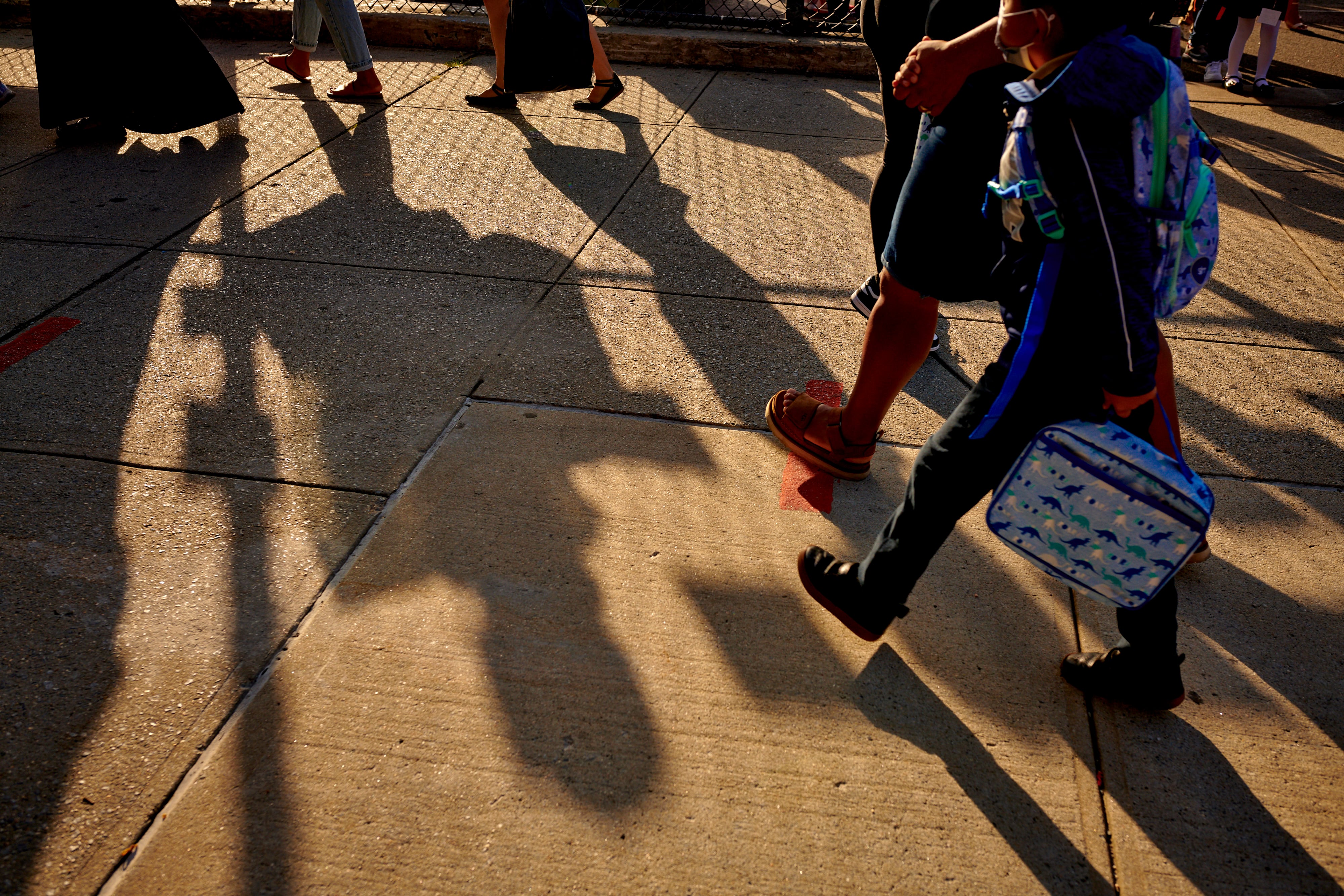 Shadows of students walking to school on a concrete walkway.