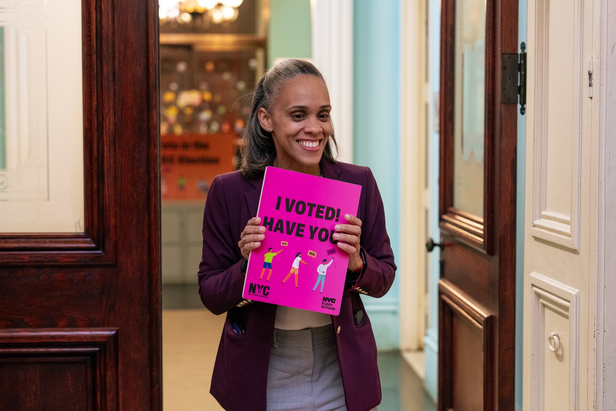 A photograph of a woman holding a pink piece of paper and smiling while walking through a door frame.