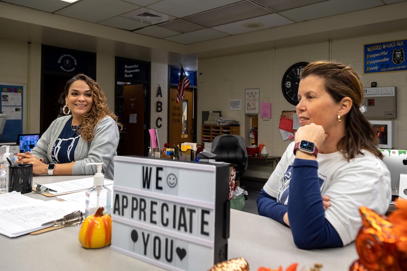 Two women stand at a desk in a school office.