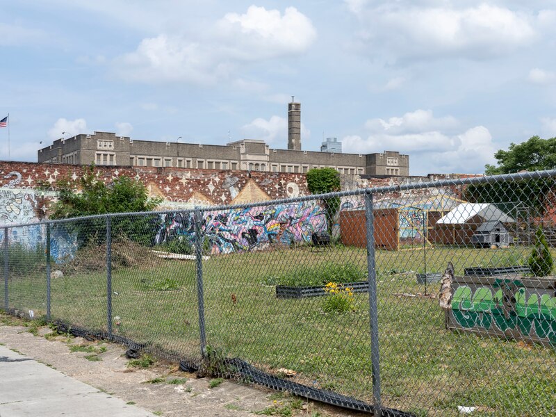 A school building with lots of graffiti on the side and a metal fence in the foreground.