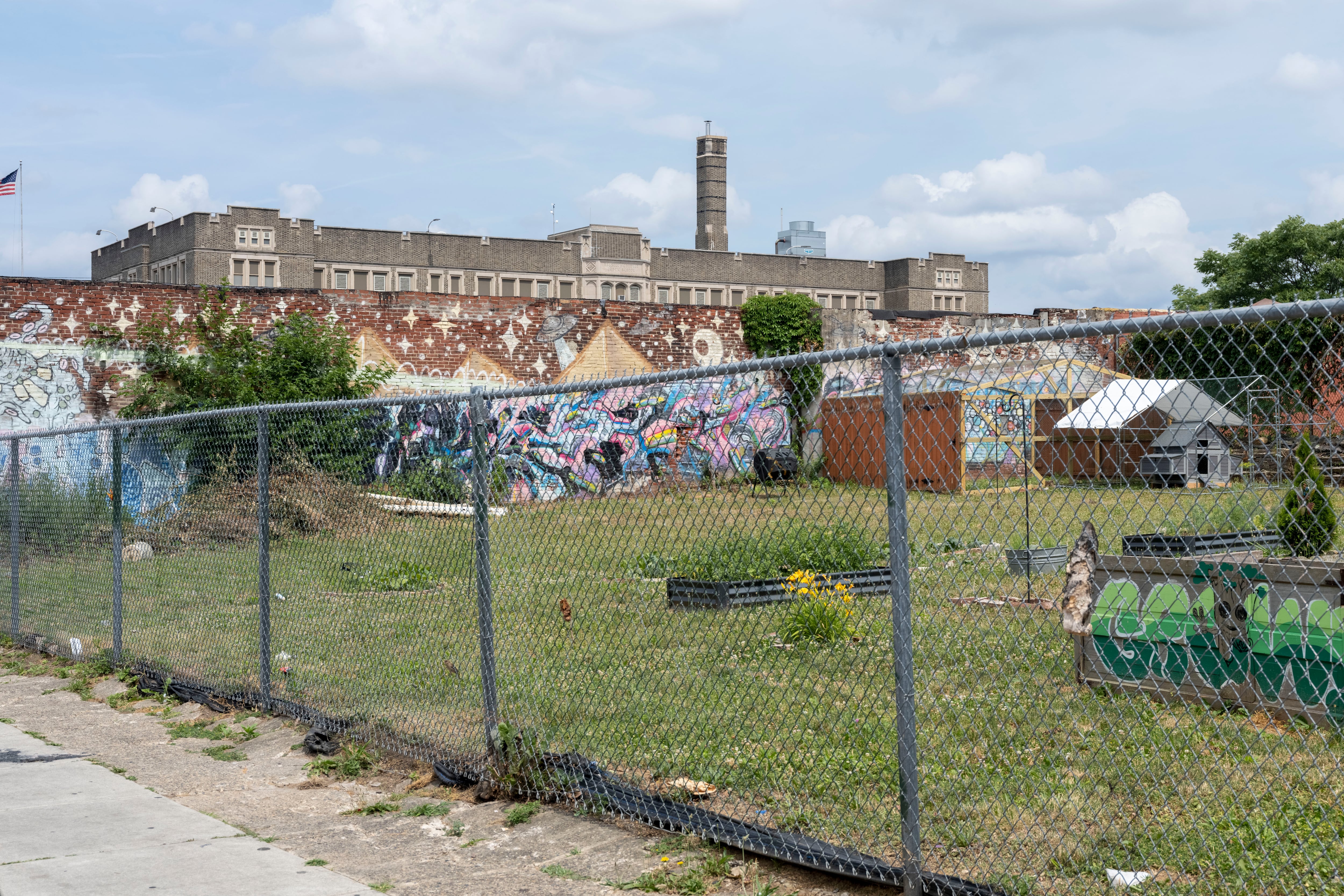 A school building with lots of graffiti on the side and a metal fence in the foreground.