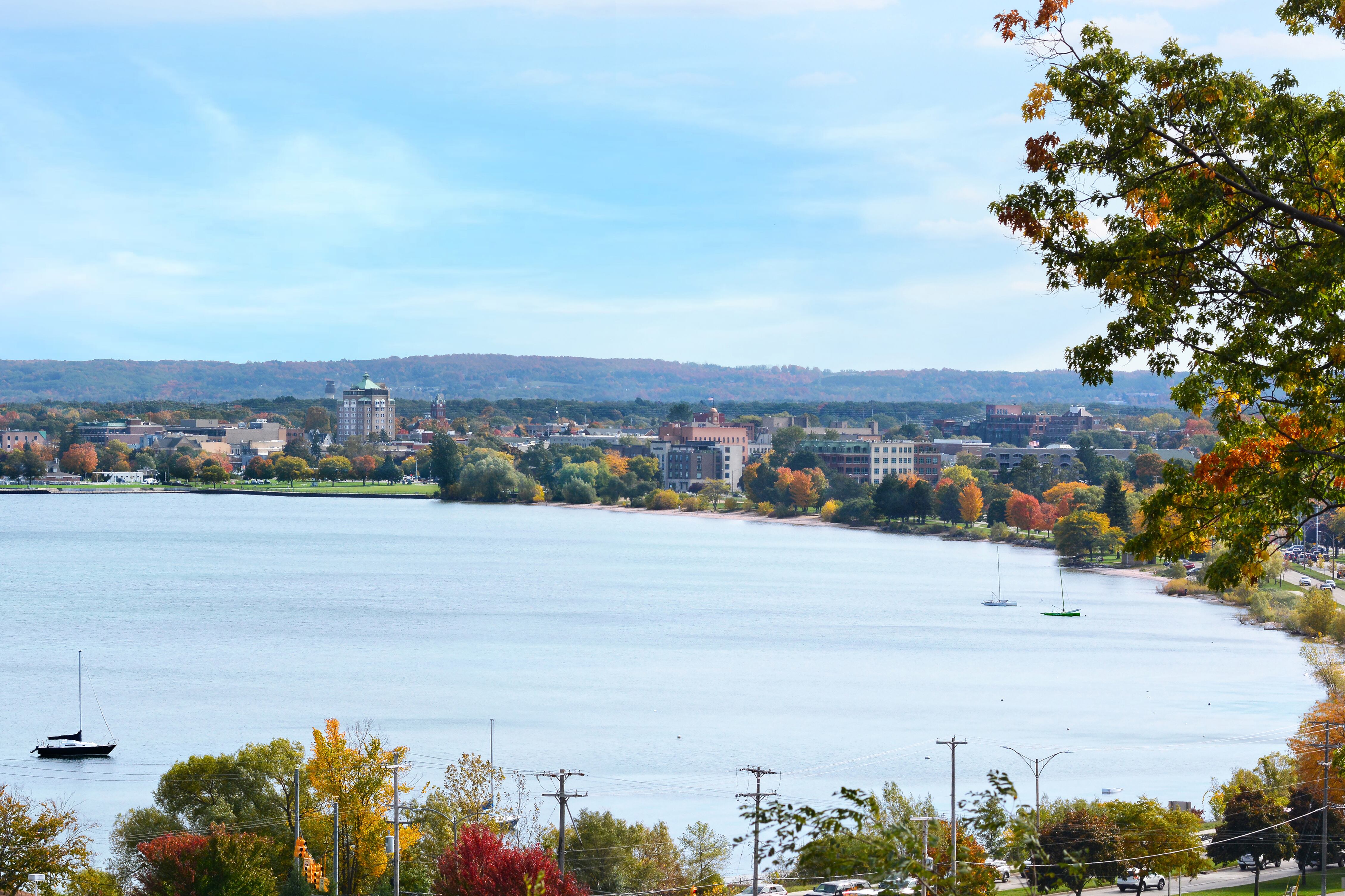 Three sail boats in a bay with fall foliage and a town in a background.