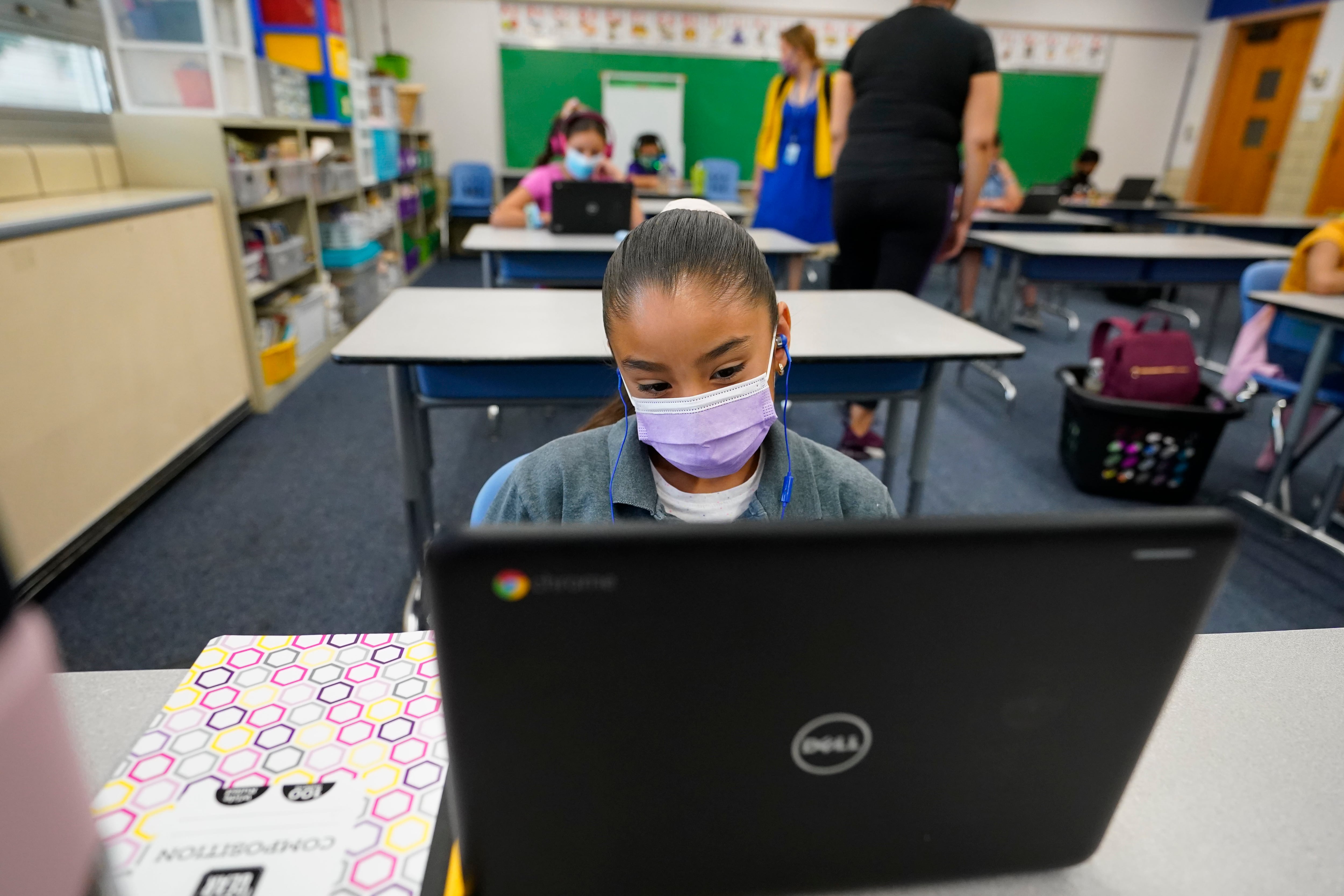 A masked girl works on her laptop at a learning center.