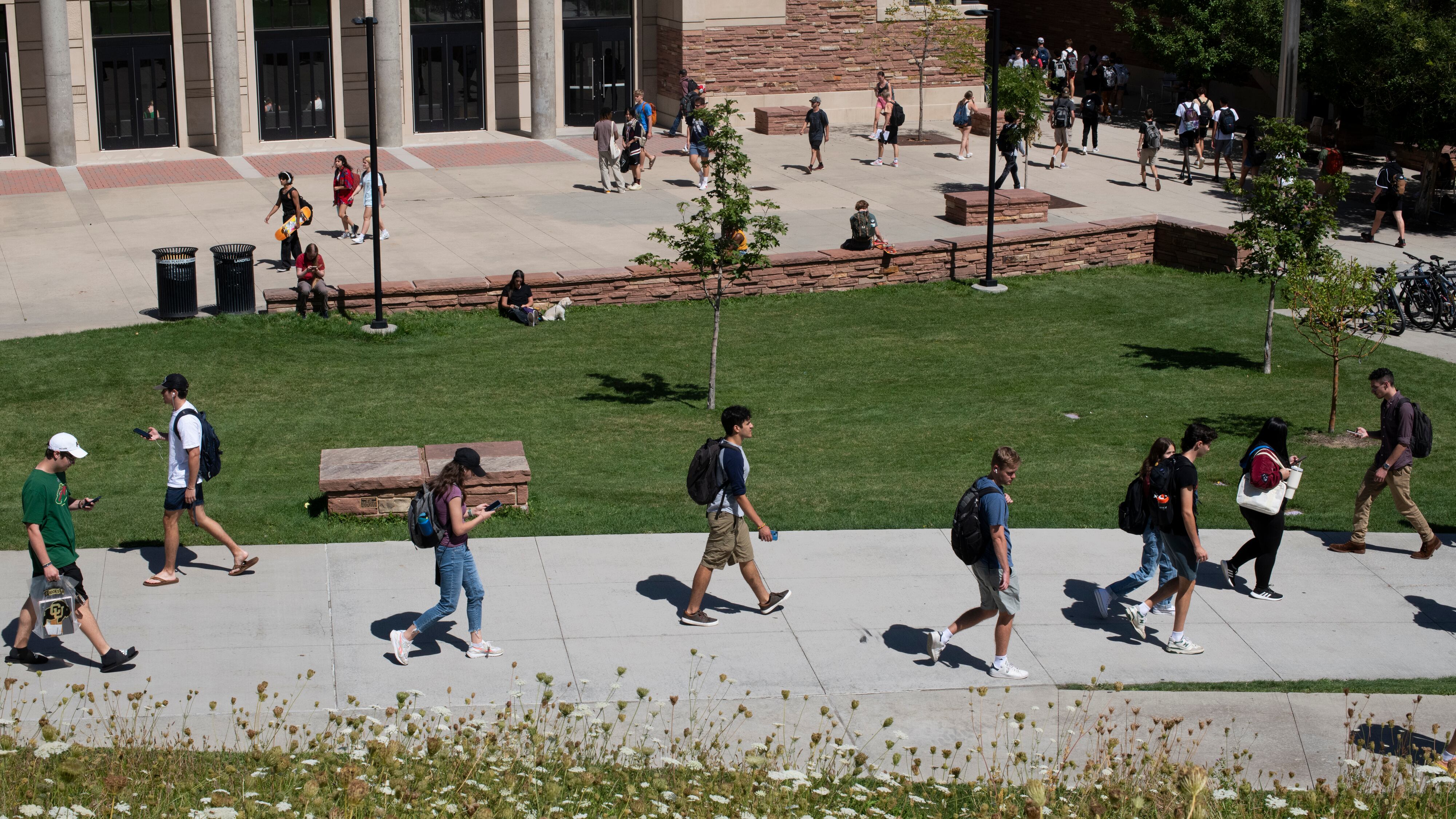 Students walk on a sidewalk path with brick buildings in the background.