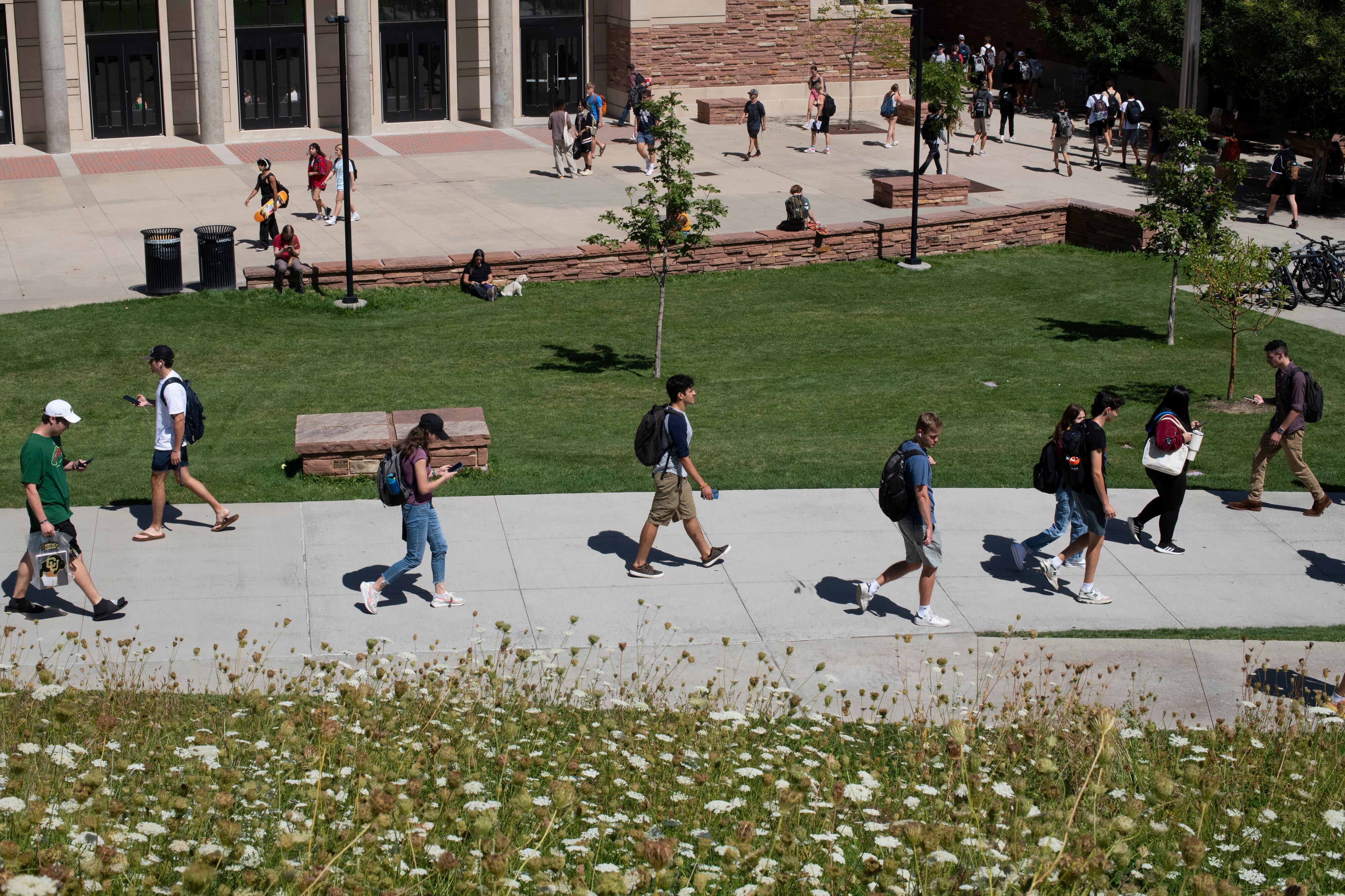 Students walk on a sidewalk path with brick buildings in the background.