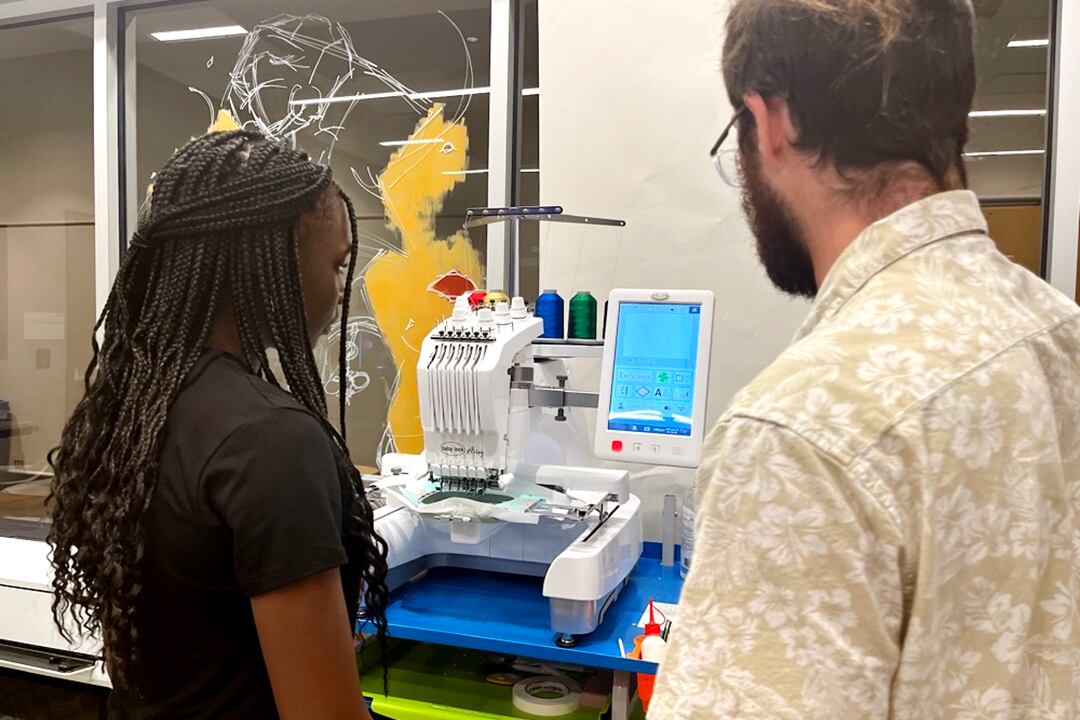 A young woman with a dark top and a man in a light shirt look at a machine.