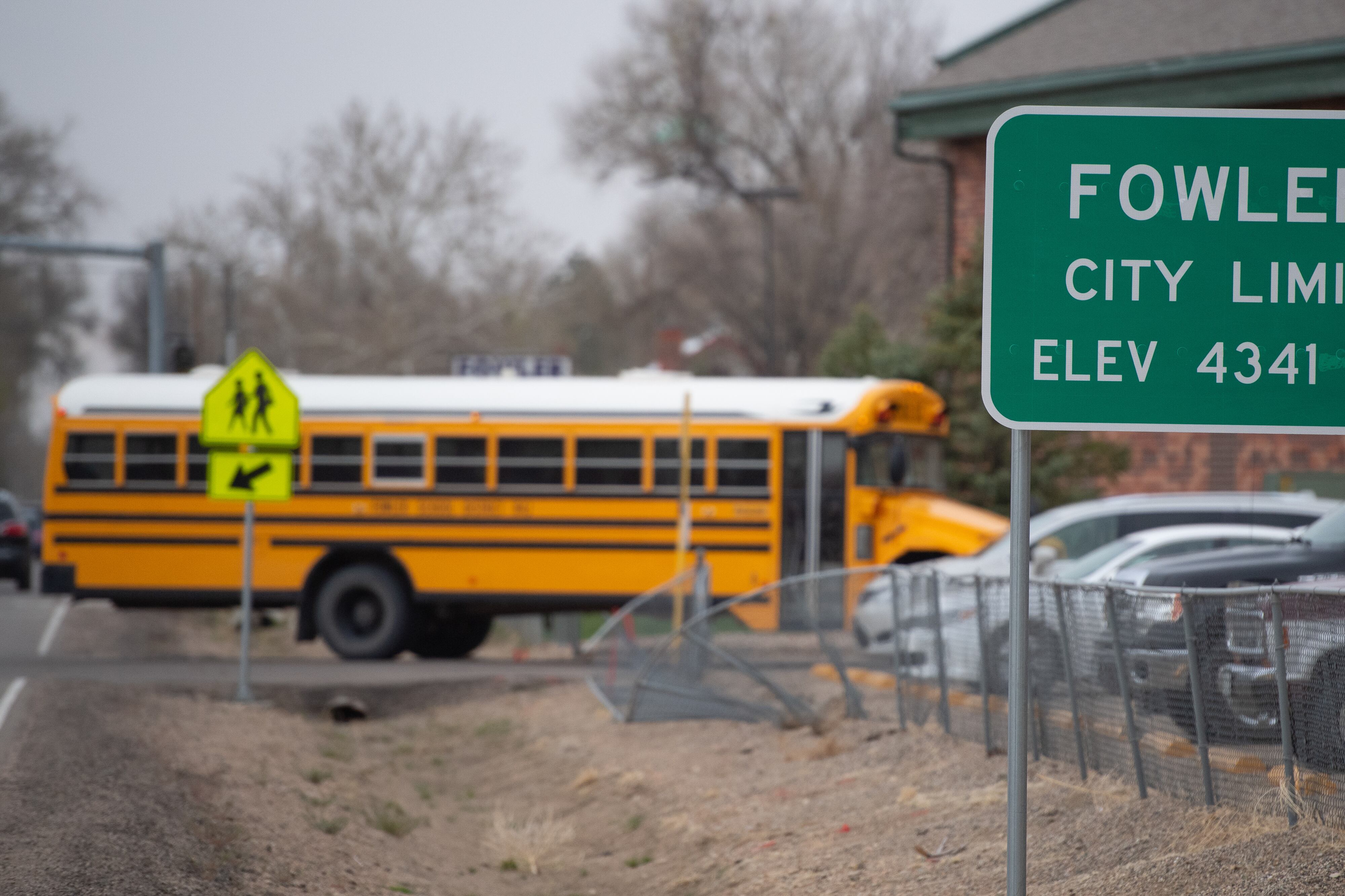 A yellow school bus enters a parking light in the background behind a sign that reads “Fowler.”