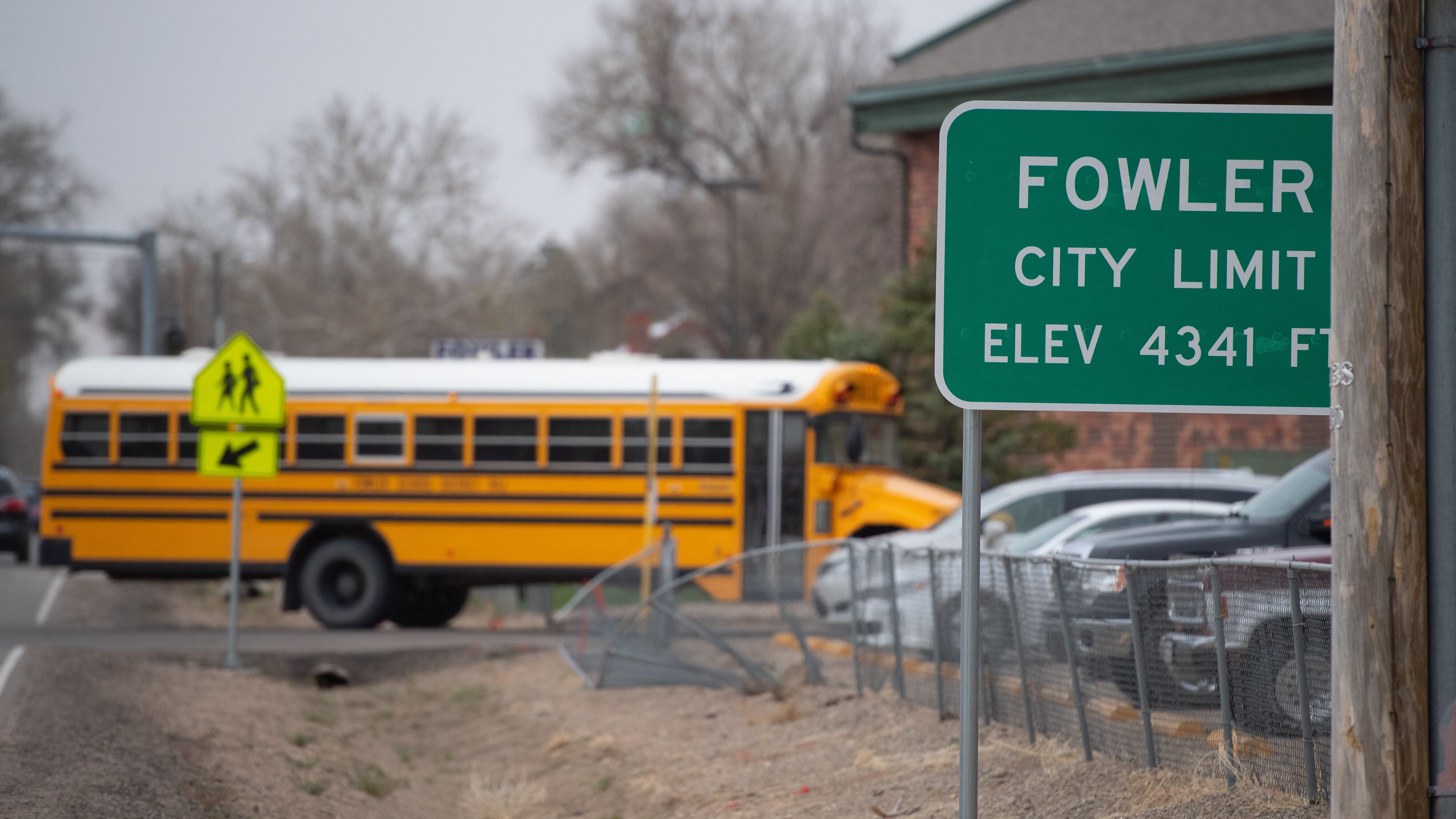 A yellow school bus enters a parking light in the background behind a sign that reads “Fowler.”
