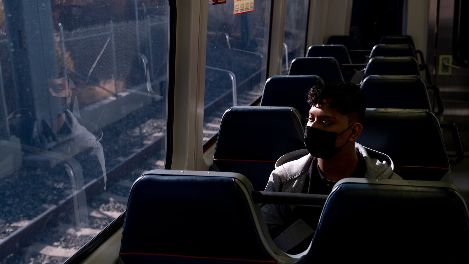The mid-morning light shines on a young man riding the train, whose reflection looks back at him in the window.