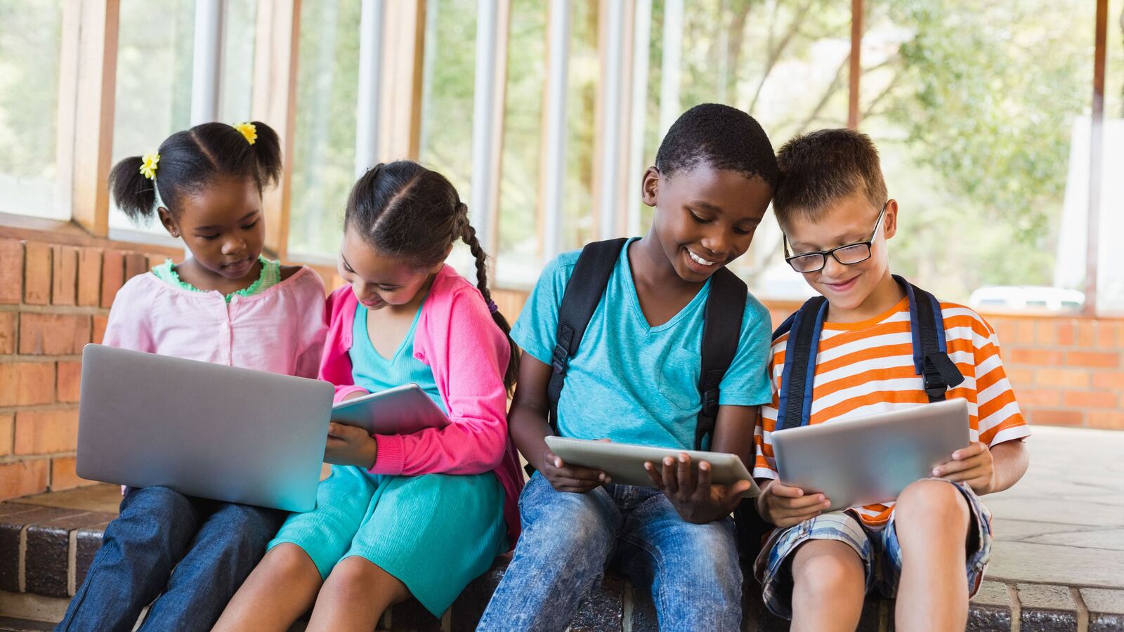 Four grade-school students sit together looking at laptops and work on school work.