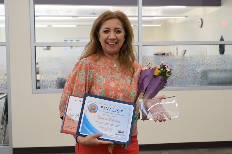 A woman in a multi-colored top holds documents and flowers.