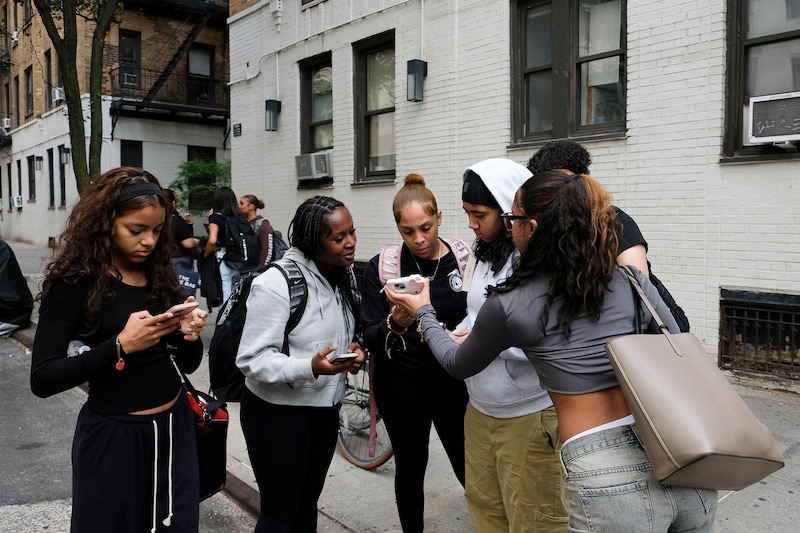 A photograph of a group of high school students holding their cellphones outside of a buiding.