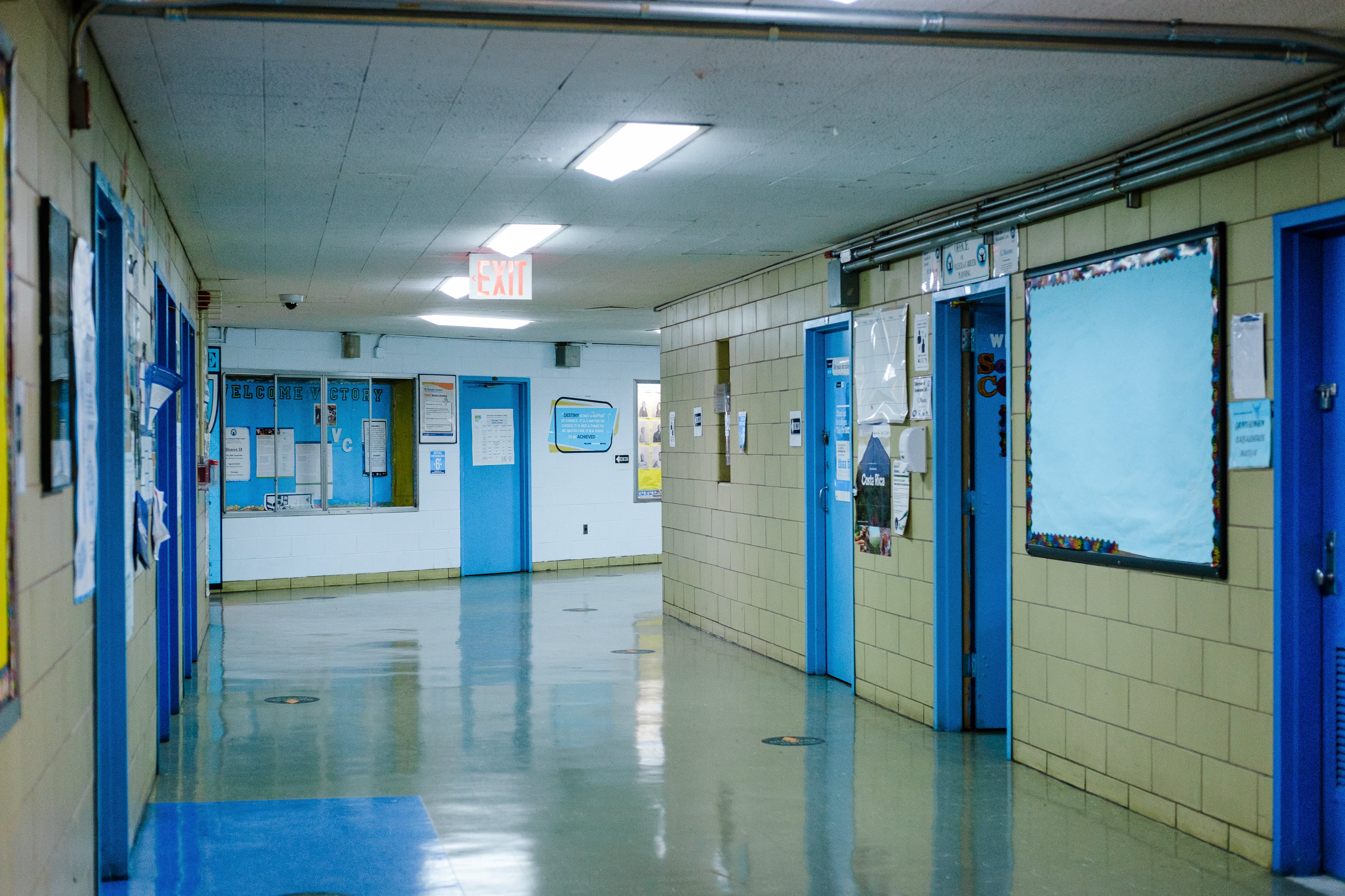 An empty school hallway with beige walls and blue doors