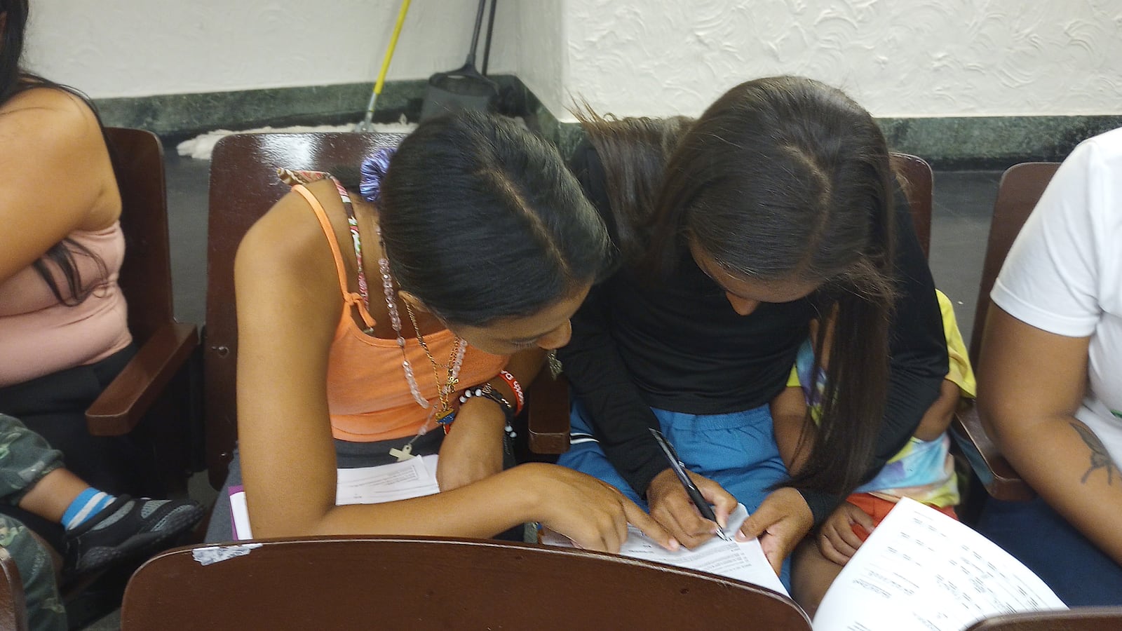 Two teenage girls huddle as they fill out paperwork.
