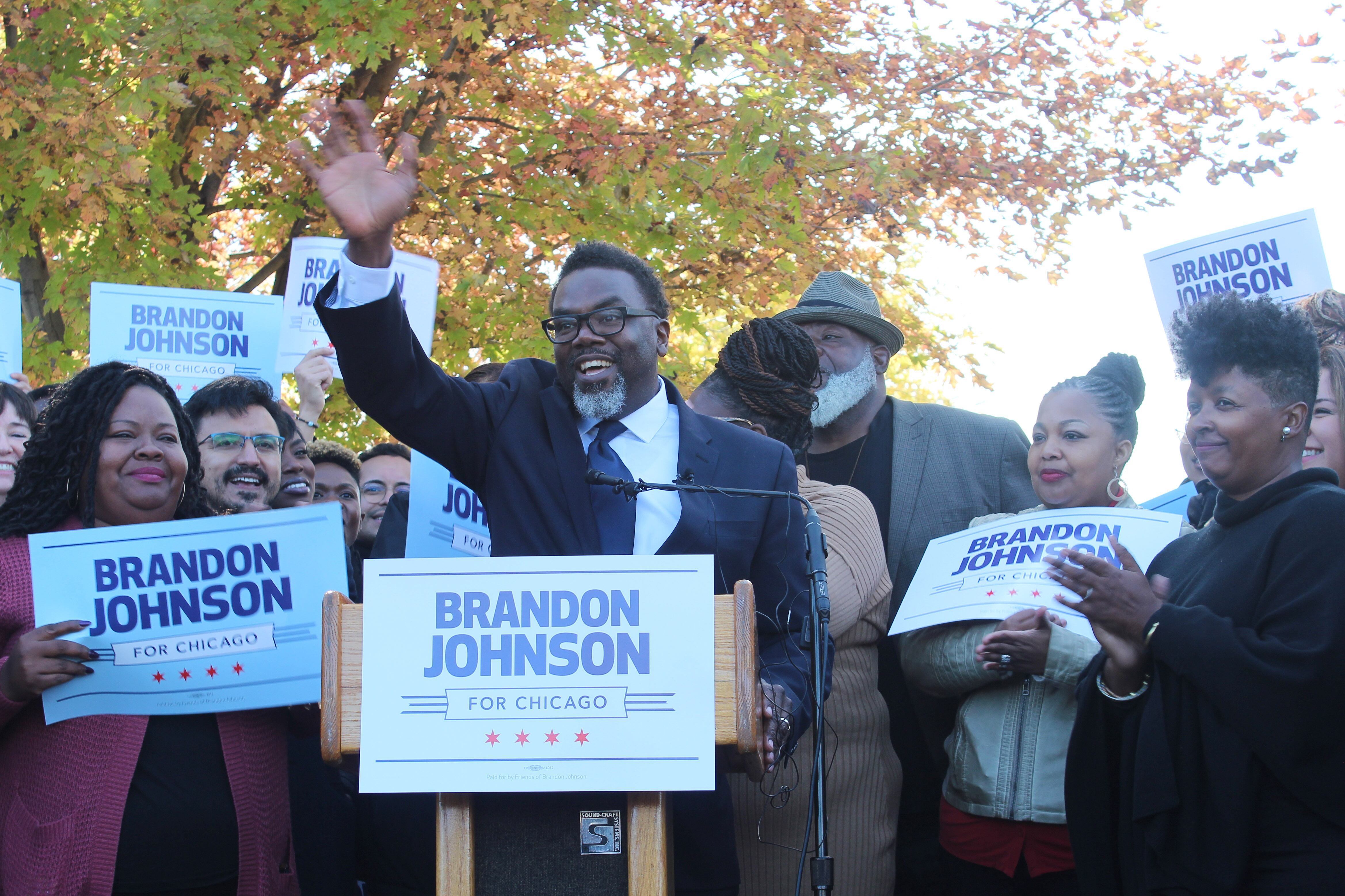 Man in suit raises right hand surrounded by supporters