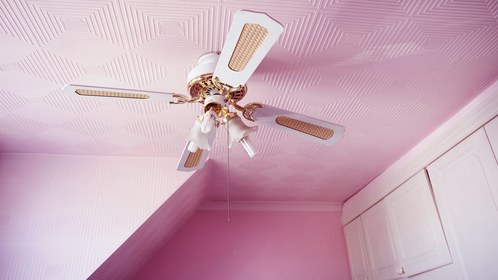 Photo of a pink bedroom with a ceiling fan and white cabinets