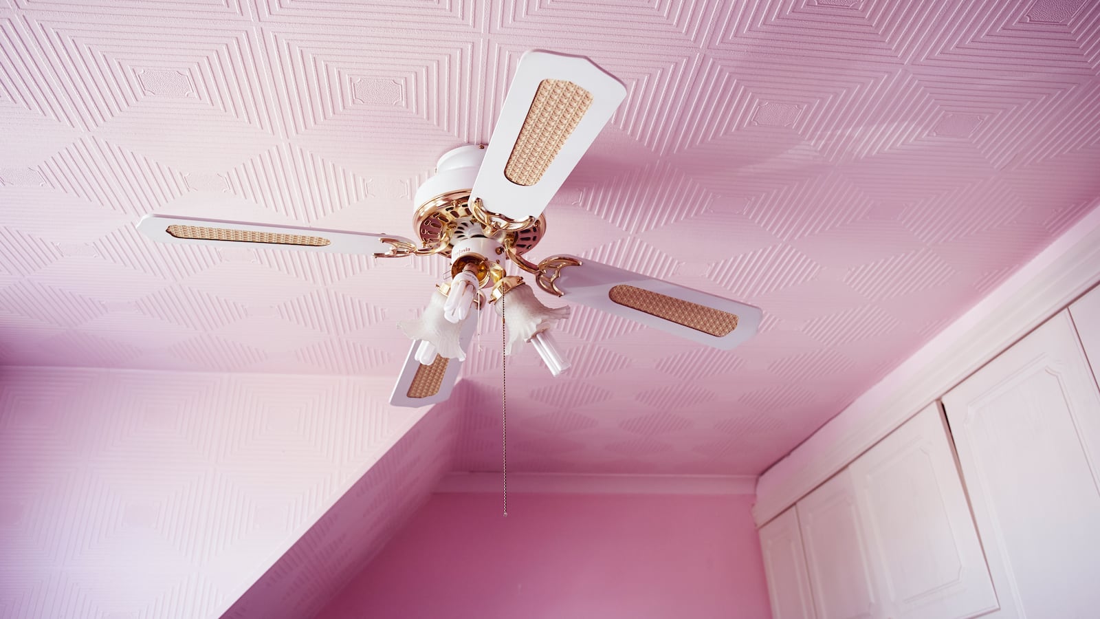 Photo of a pink bedroom with a ceiling fan and white cabinets