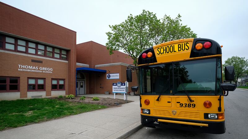 A yellow school bus is parked in front of the brick building of Thomas Gregg Neighborhood School in Indianapolis, Ind.