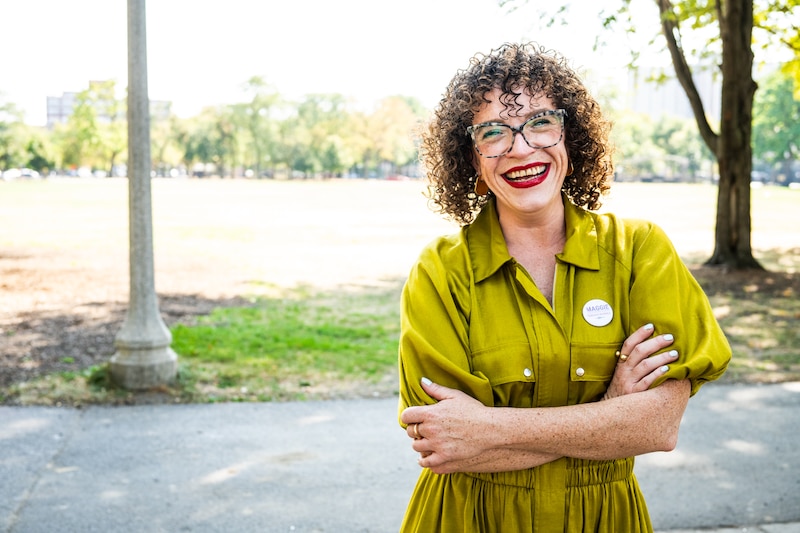 A woman in a chartreuse dress stands in front of a sidewalk.