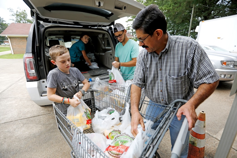 Adults and children load groceries from a cart into the back of a minivan.