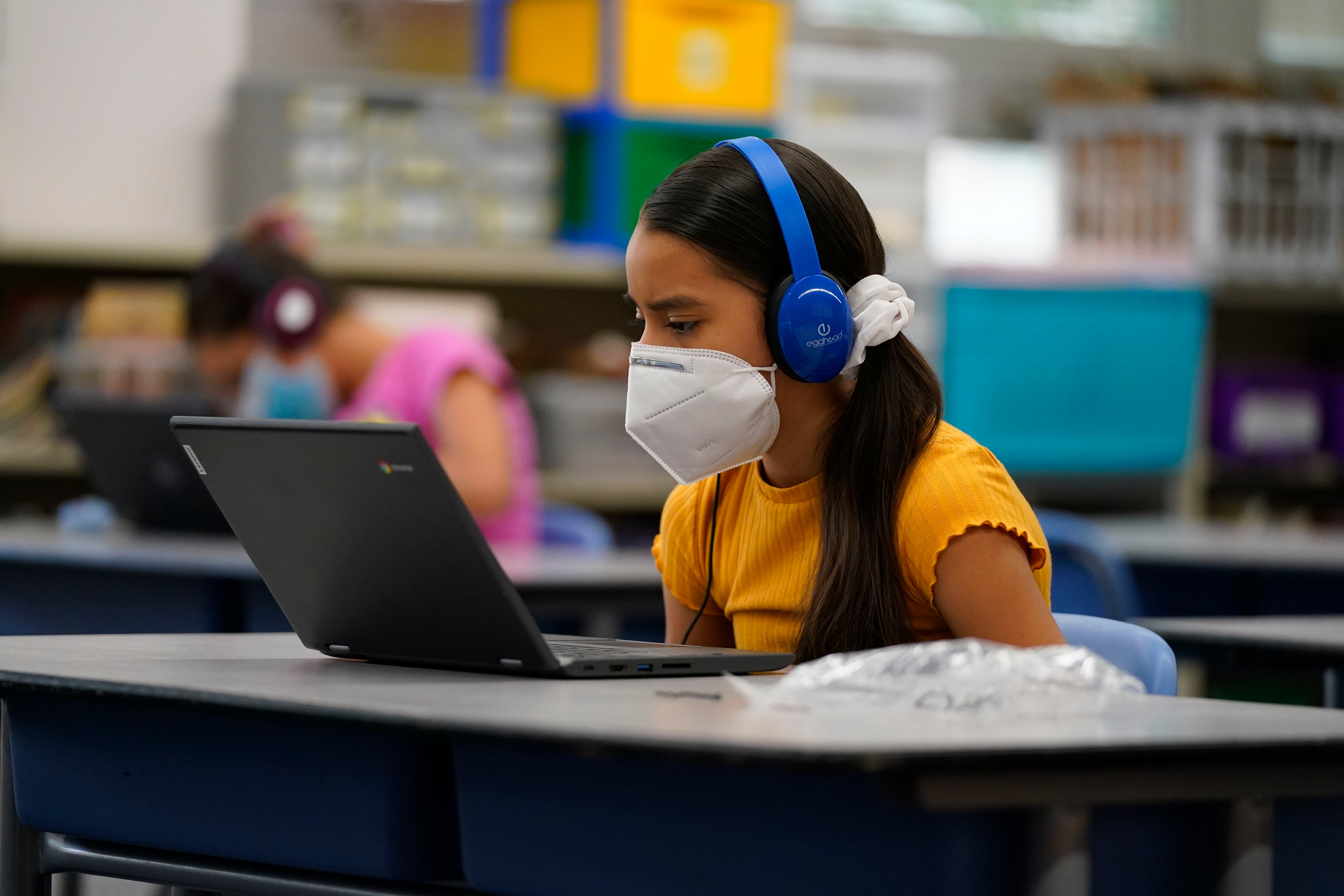 Girl wearing a mask works on her laptop at a learning center.
