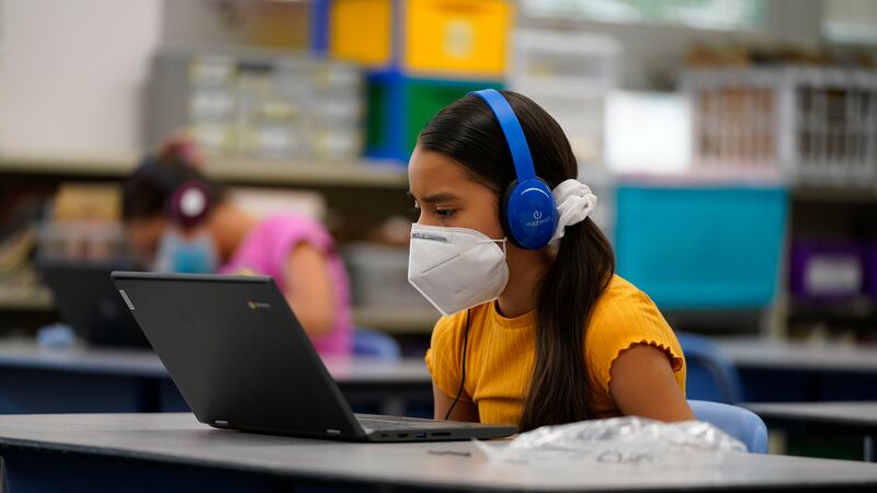 Girl wearing a mask works on her laptop at a learning center.
