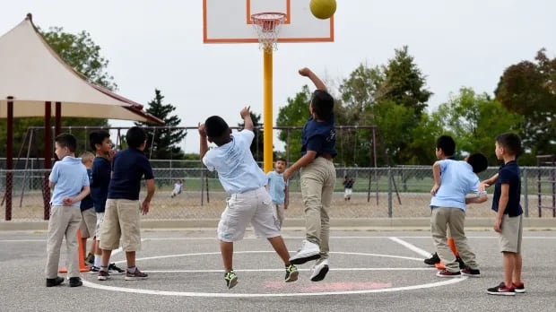 Young boys in blue shirts and khaki pants or short play basketball on an outdoor court.
