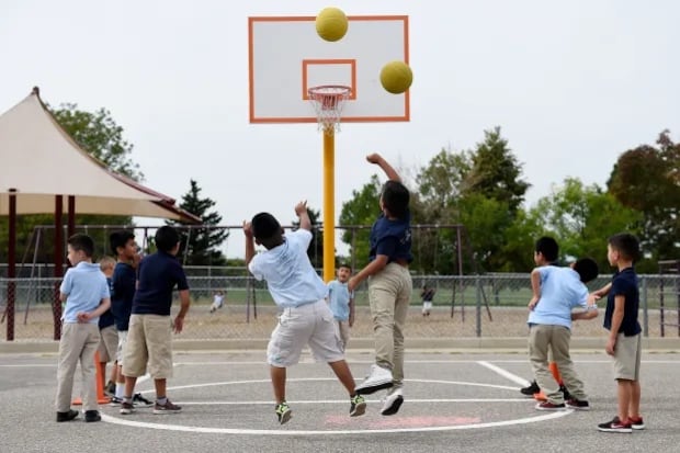 Young boys in blue shirts and khaki pants or short play basketball on an outdoor court.