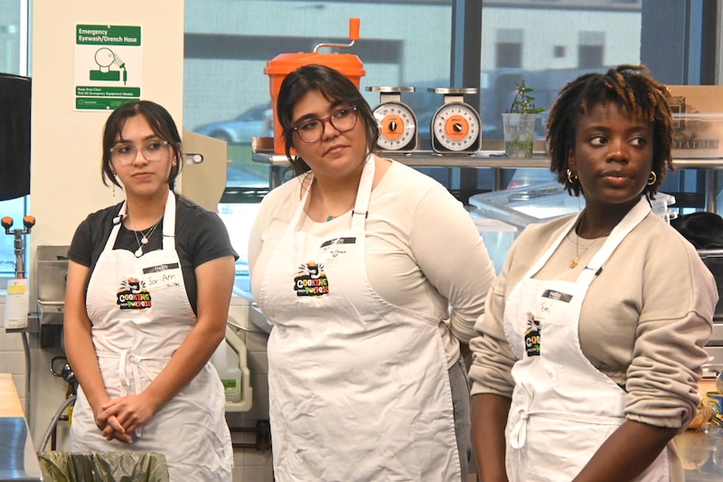 Three women with aprons stand together.