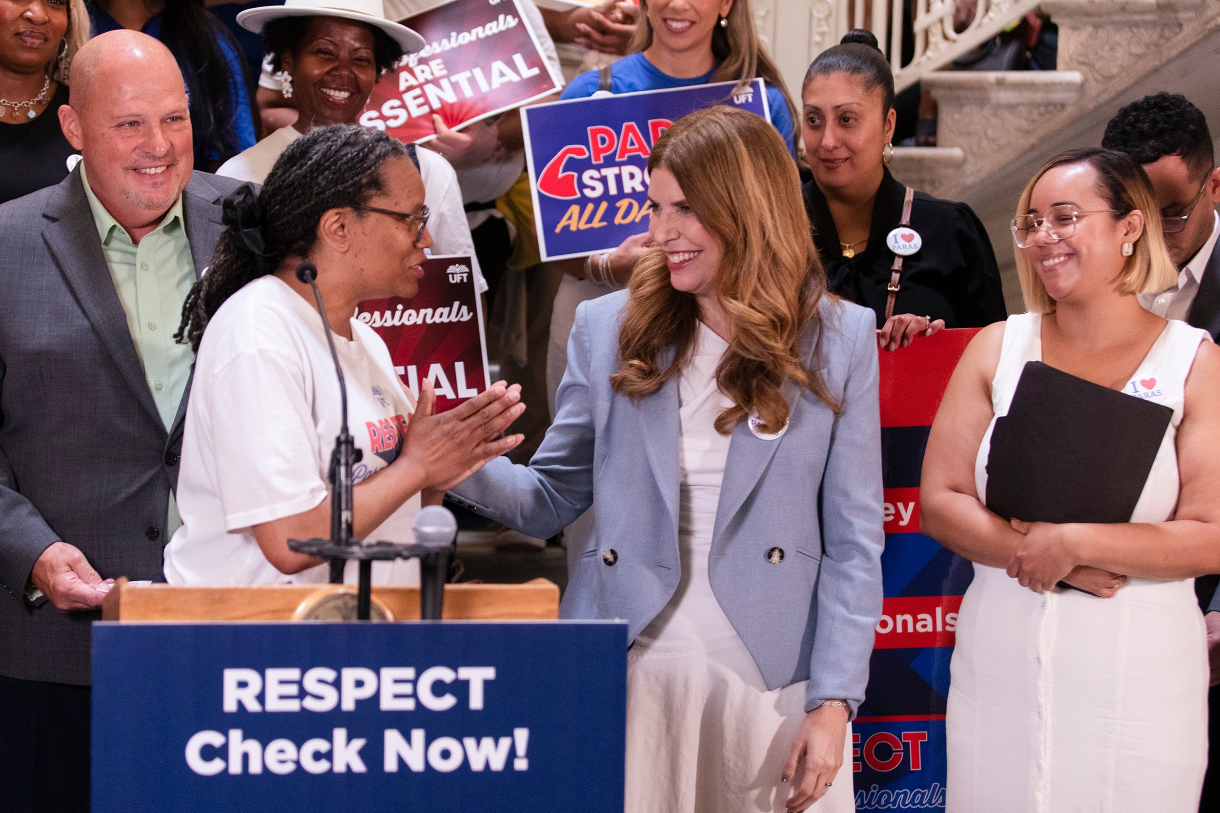 Three women and one man stand behind a wooden podium during a press conference.