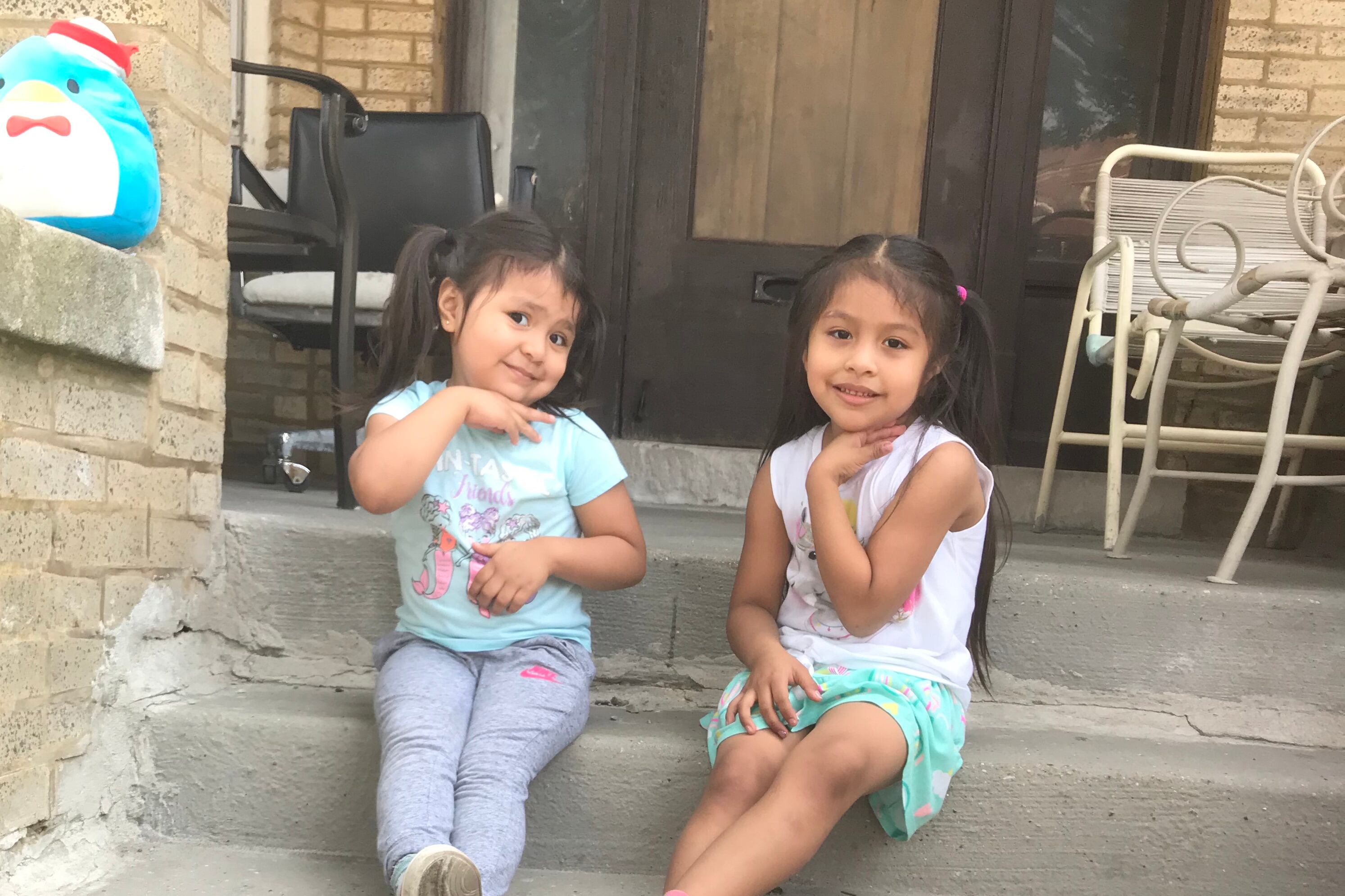 Two young girls sit on the front porch of their Chicago home. Their mother worries about who will care for them if their preschool closes. 