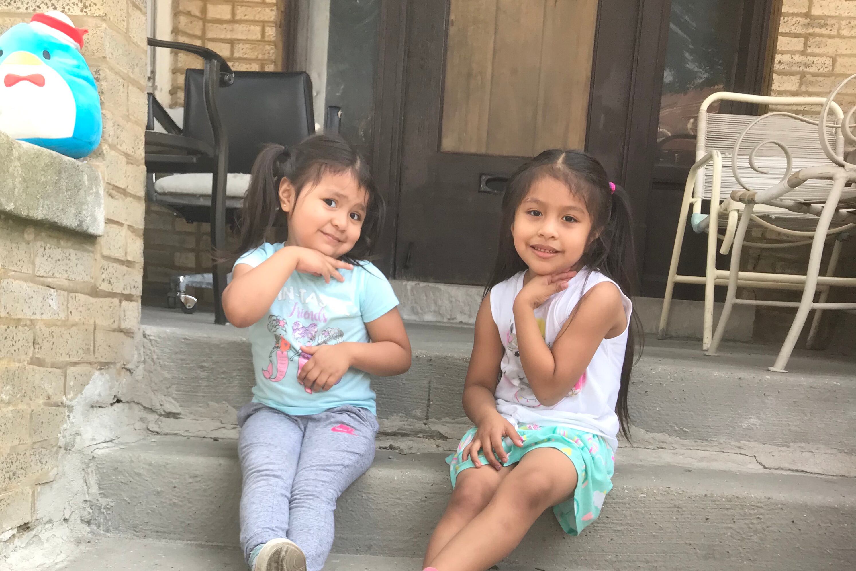 Two young girls sit on the front porch of their Chicago home. Their mother worries about who will care for them if their preschool closes.