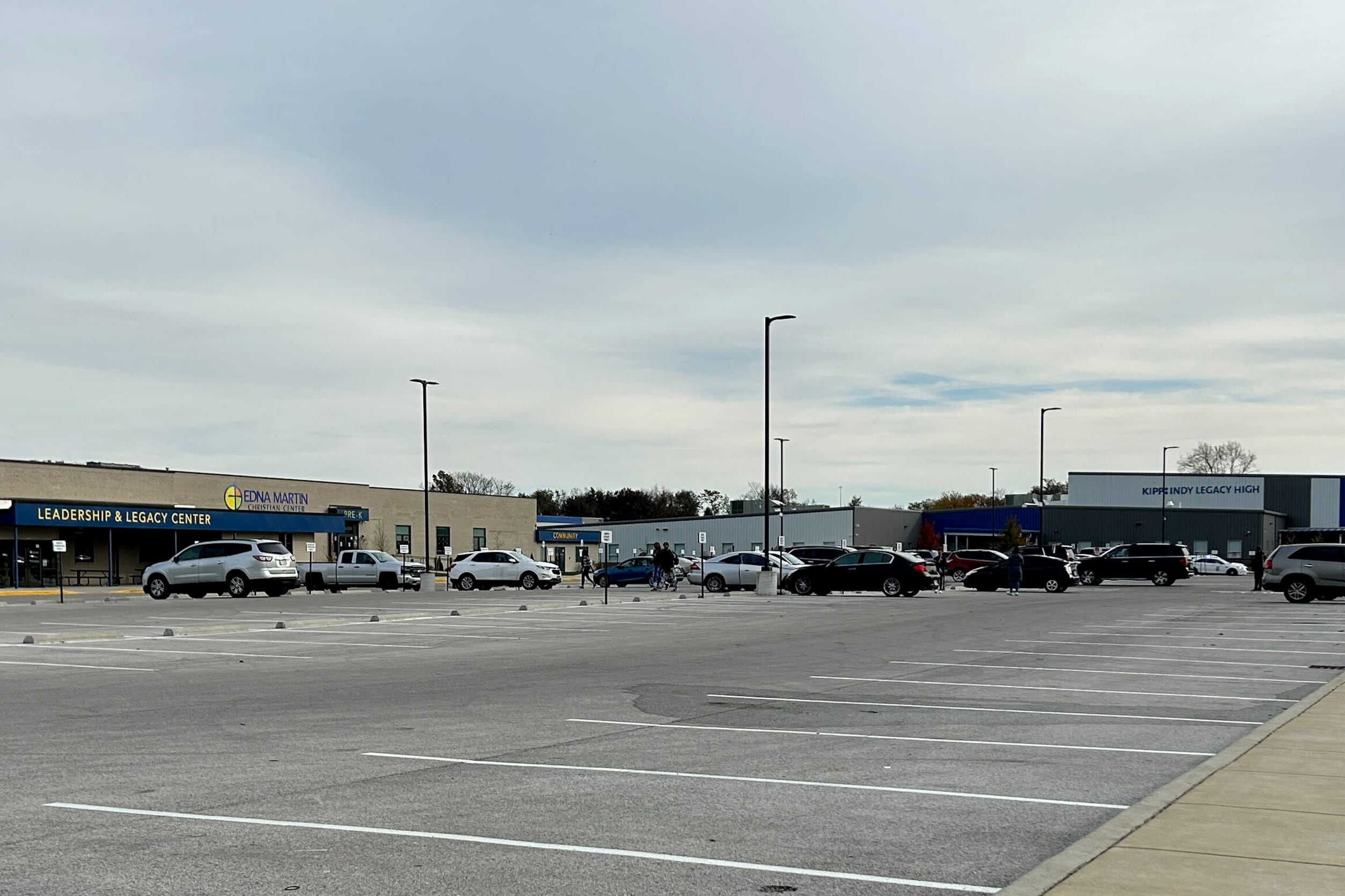 A parking lot with a liquic stain in the immediate foreground. In the background is high school building with the sign “KIPP Indy Legacy High.”