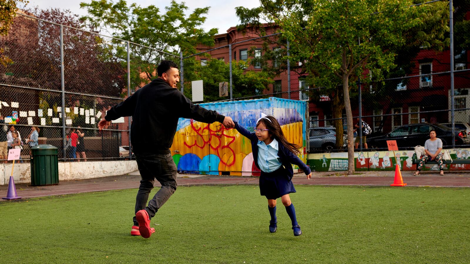A father and daughter play on a small turf field together.
