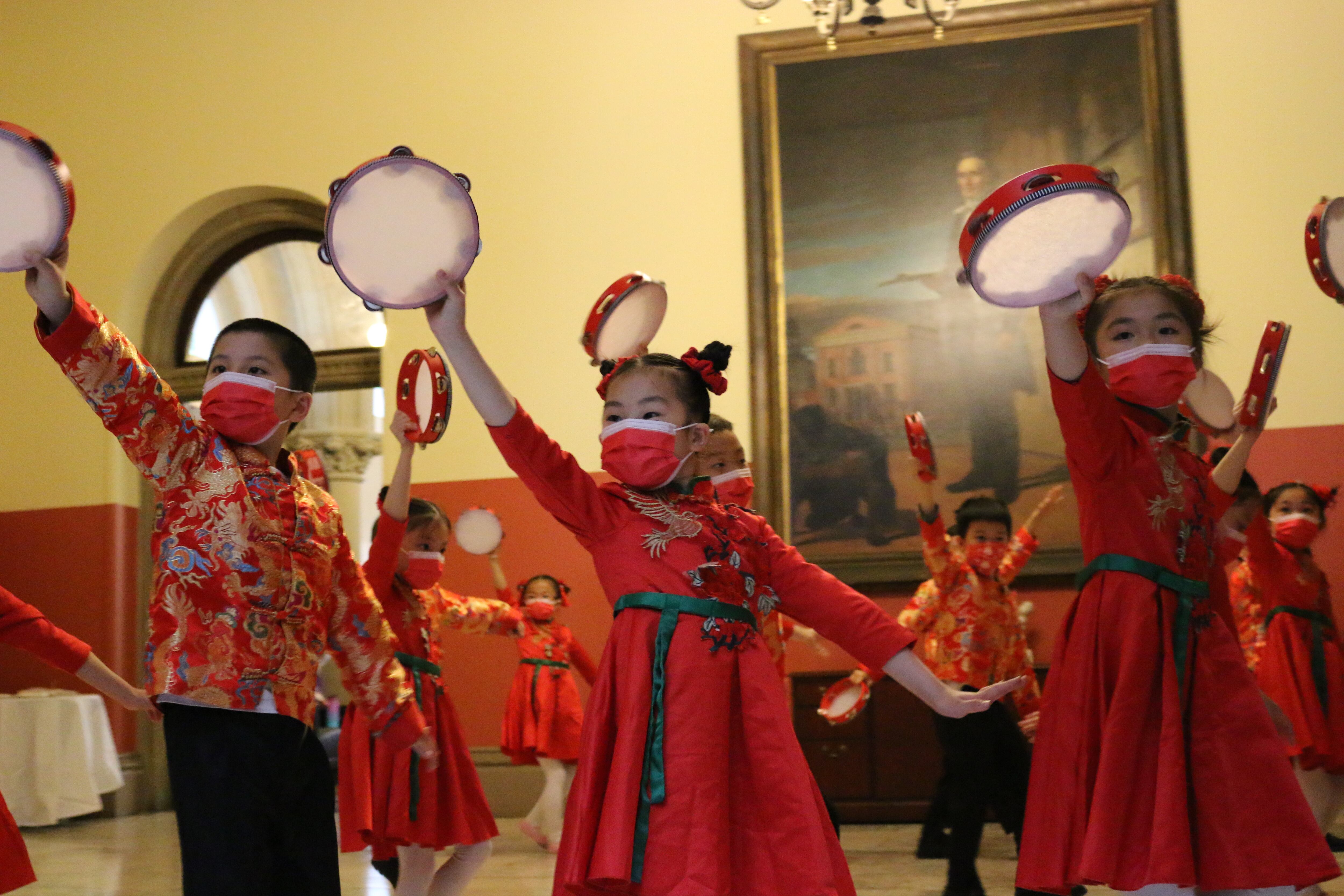 Students in red costumes and masks hold tambourines in the air.