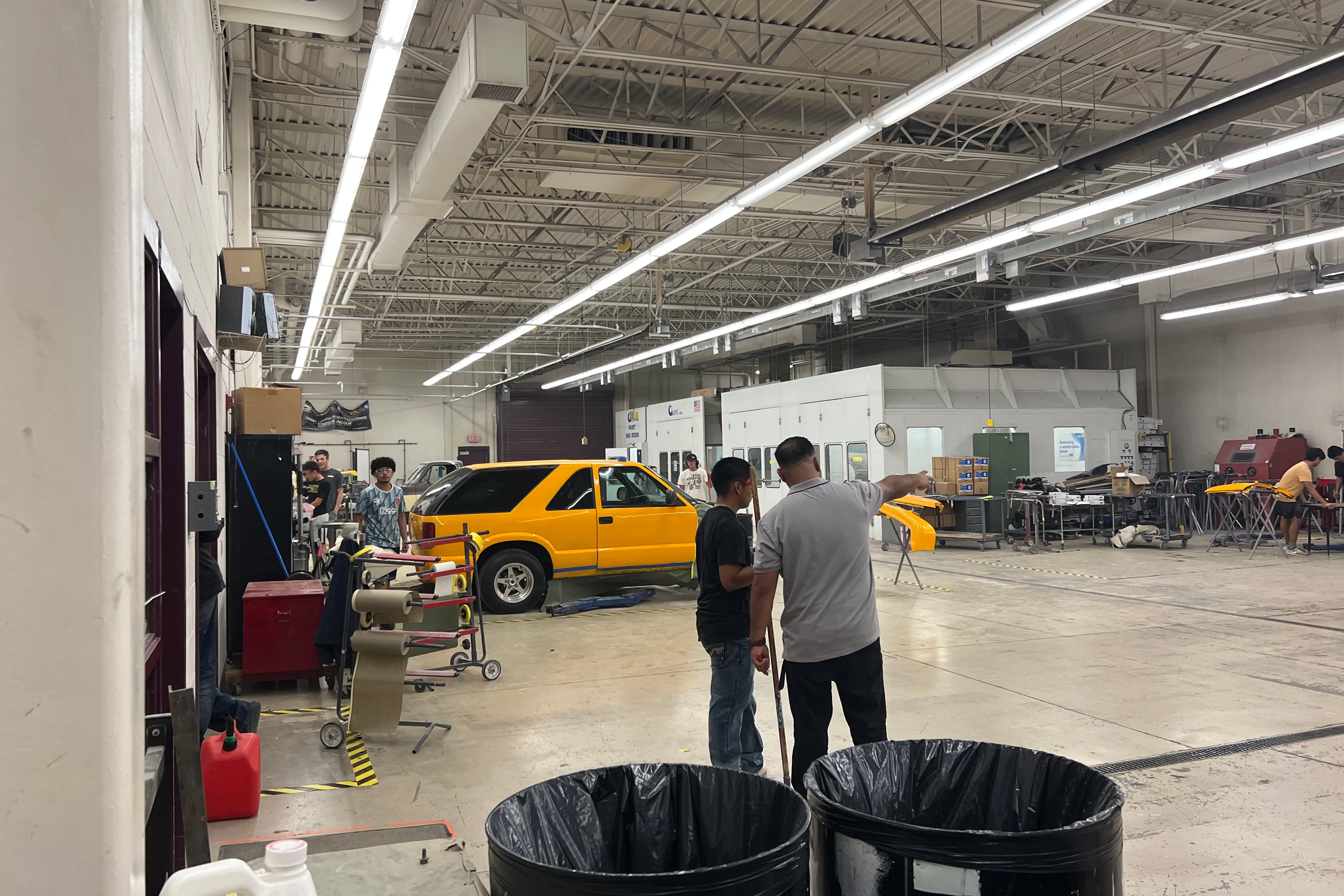An instructor and student in an automotive garage. There is a yellow SUV in the background.