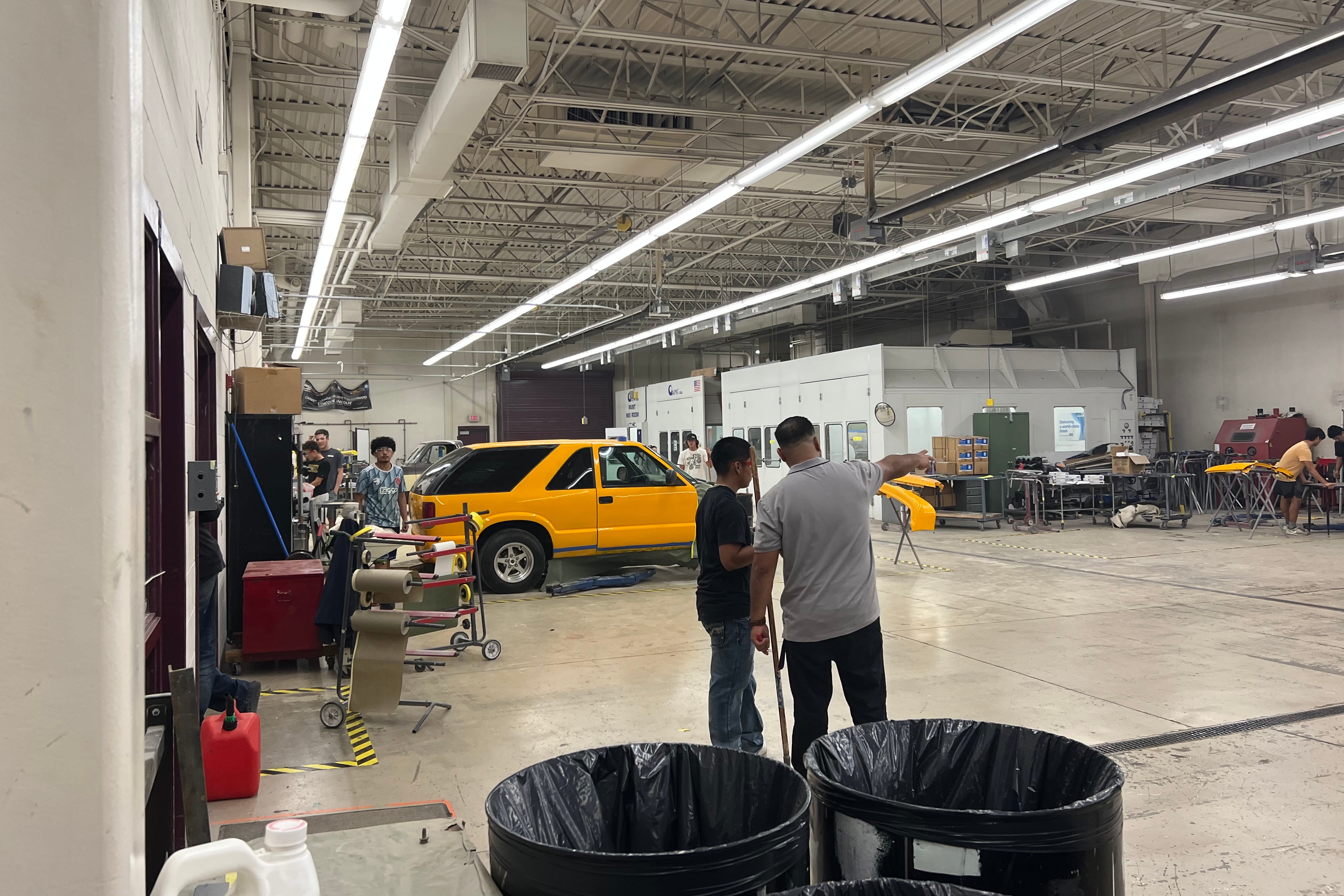 An instructor and student in an automotive garage. There is a yellow SUV in the background.