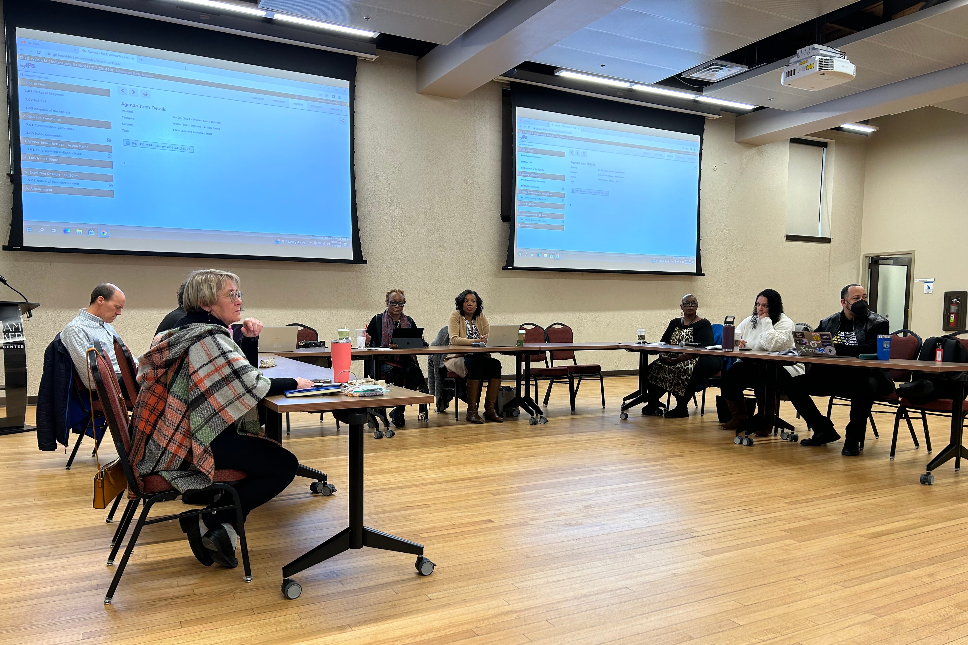 A group of people sit around three tables in a rectangular shape.