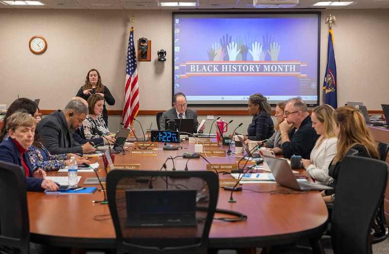 A group of people in business clothes sit at a wooden table in a conference room.